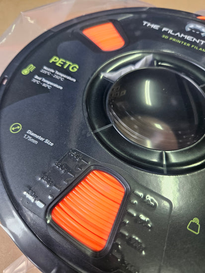 Close-up of a spool of PETG filament with orange pull tab on a clear background