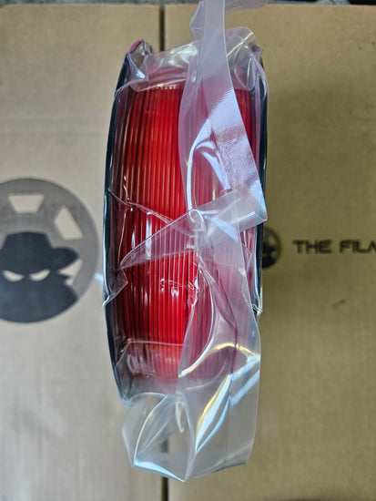 Red spool of wire in clear plastic wrap on a cardboard surface