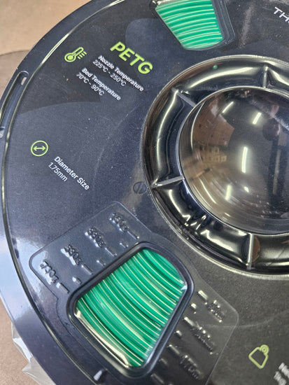 Close-up of a 3D printing filament spool with PETG label and green filament.