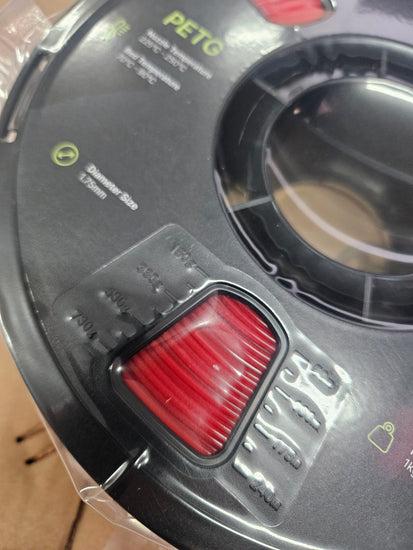 Close-up of a spool of PETG filament with a red stripe on a clear plastic packaging.