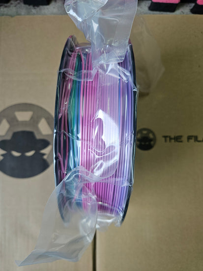 Spool of colorful wire on a clear plastic wrap against a cardboard background