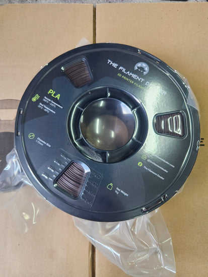 Spool of filament labeled 'The Filament' on a cardboard surface