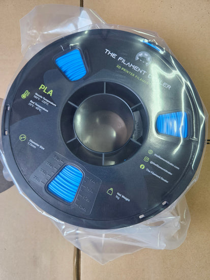 Spool of filament with blue accents on a clear plastic stand against a beige background