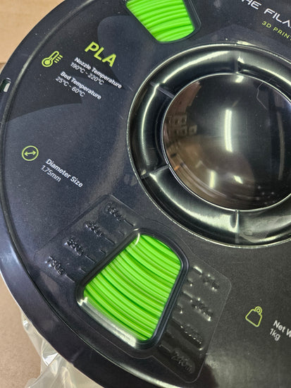 Close-up of a spool of PLA filament with green accents on a black background.