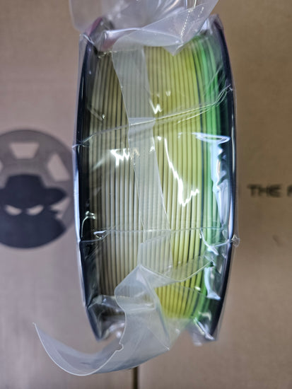 Spool of green and yellow wire in clear plastic packaging on a cardboard background