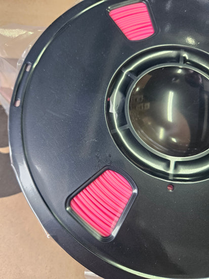 Close-up of a black circular object with pink filters on a clear stand.