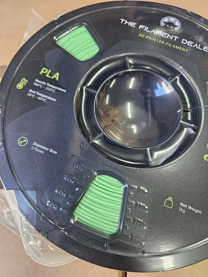 Spool of green filament with 'The Filament Dealer' branding on a beige background