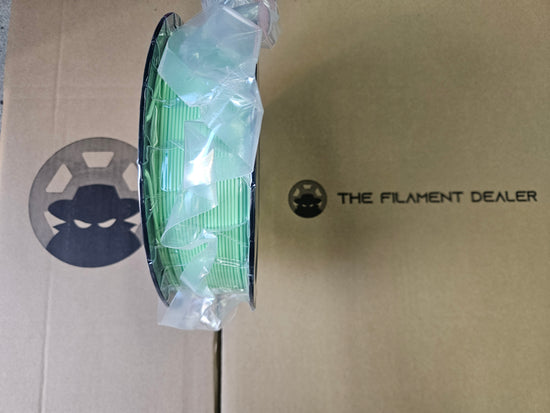 Spool of green filament on a cardboard box with 'The Filament Dealer' branding.