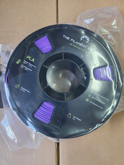 Spool of filament with purple ends on a clear plastic stand against a cardboard background