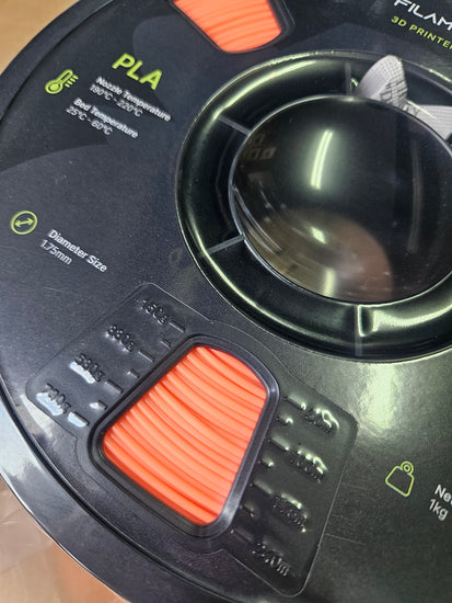 Close-up of a 3D printer filament spool with PLA label and orange button.